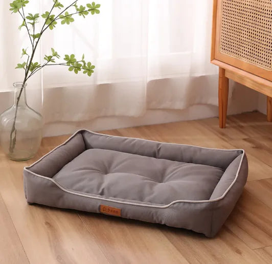 Gray pet bed on a wooden floor with a vase and plant in the background